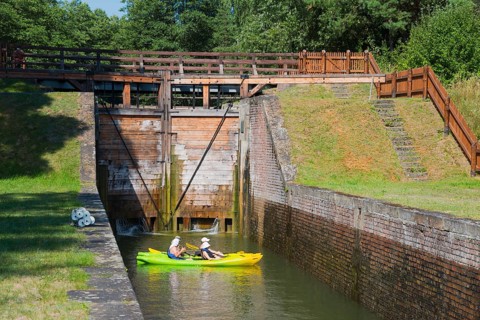 Two yellow kayaks in a canal in front of a closed lock with green and quiet surroundings, Sluza