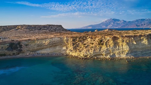 Rocky coast with bright sunshine and blue sky by the sea, drone shot, evening light, Paralia Agios