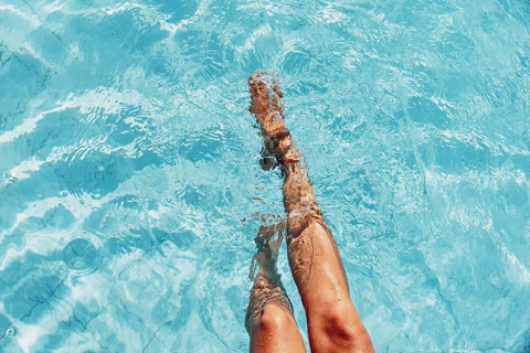 Two legs dipping in the sunny blue pool water, relaxed atmosphere