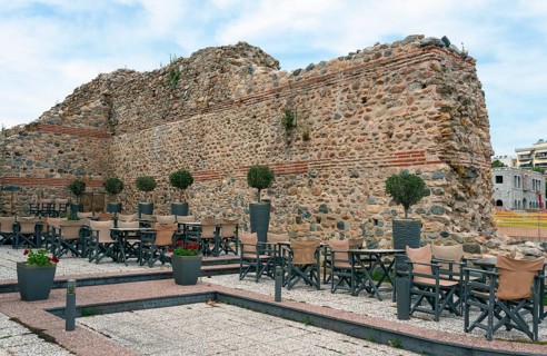 A street café in front of the ruins of an old wall under a partly cloudy sky in an urban historical