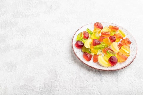 Various fruit jelly candies on plate on gray concrete background. side view, copy space