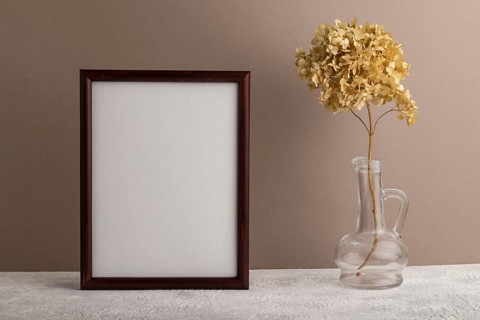 Brown wooden frame mockup with dried hydrangea in glass on beige paper background. Blank, vertical