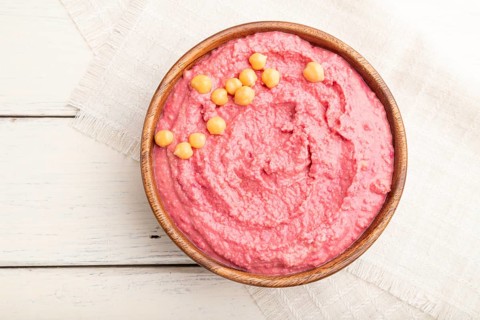 Hummus with beet in wooden bowl on a white wooden background and linen textile. Top view, flat lay,