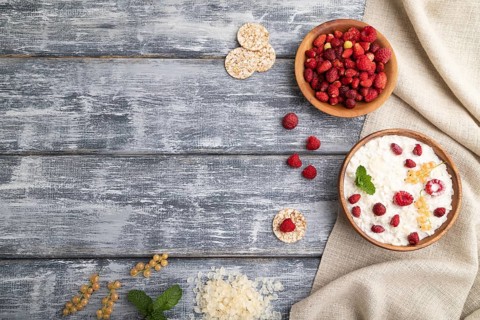 Rice flakes porridge with milk and strawberry in wooden bowl on gray wooden background and linen