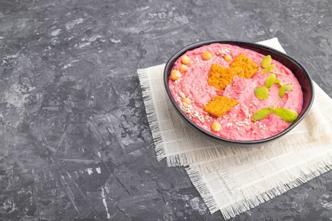 Hummus with beet and microgreen basil sprouts in ceramic bowl on a black concrete background and