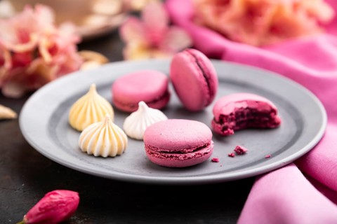 Purple macarons or macaroons cakes with cup of coffee on a black concrete background and pink