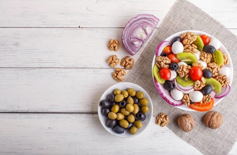 Salad with fresh cherry tomatoes, mozzarella cheese, olives, kiwi, onion and walnuts on white