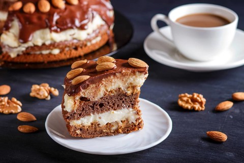 Homemade chocolate cake with milk cream, caramel and almonds on black wooden background. cup of