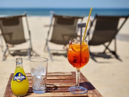 A bottle of Orangina, a glass with ice cube cubes and a glass of Aperol Spritz with a straw in a