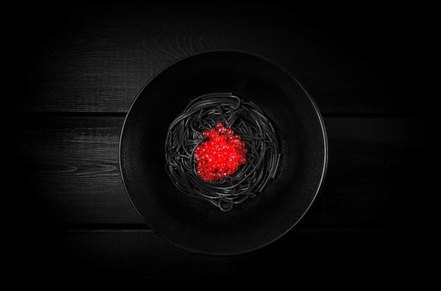 Black spaghetti with red caviar, pasta, on a black background, top view, no people
