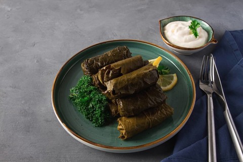 Dolma, cabbage rolls, grape leaves with filling, white sauce, lemon and herbs, rustic, selective