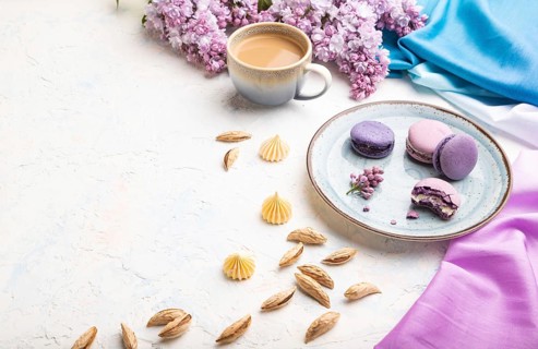 Purple macarons or macaroons cakes with cup of coffee on a white concrete background and