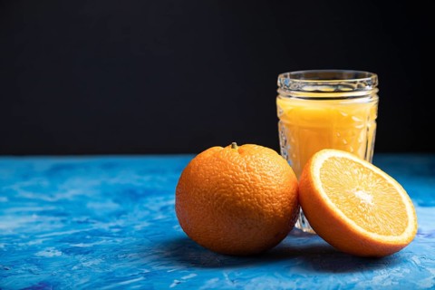 Glass of orange juice on a black and blue background. Hard light, contrast. Side view, copy space