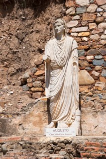 Statue of Augustus in front of a colourful stone wall, symbolising Roman history and ancient art,