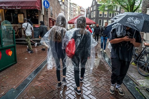 Tourists in rainy weather, with plastic ponchos, in the historic centre of Amsterdam, Netherlands