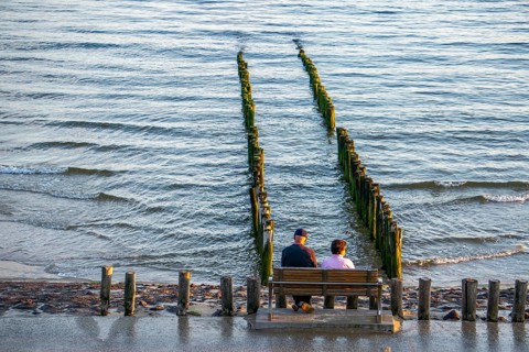 An elderly couple sitting on a bench on the beach, at high tide, breakwater, Netherlands