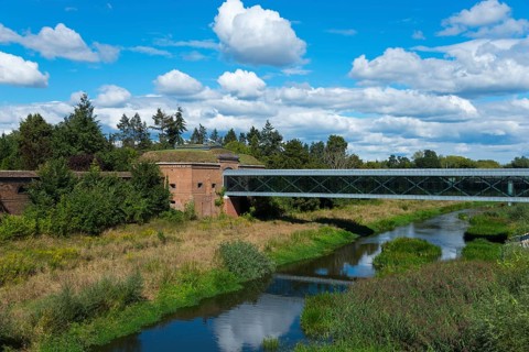 Natural landscape with a bridge over a river and lush greenery under a cloudy sky, view from the
