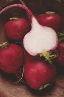 Bright red radishes lie in a rustic wooden bowl, highlighting their fresh appearance. One radish is