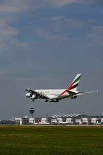 Emirates Airbus A380-800 approaching under blue sky, with control tower and Terminal 2 landing on