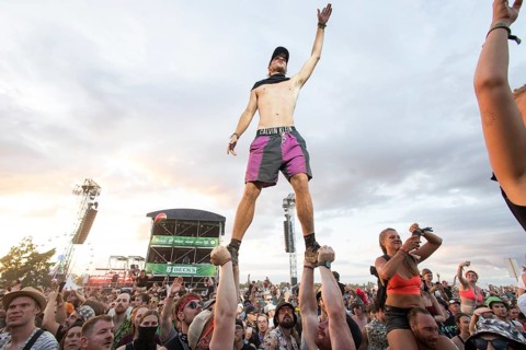 A festival visitor stands on the hands of two people during the performance of the band Feine Sahne