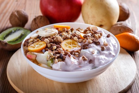 Vegetarian salad of bananas, apples, pears, kumquats, kiwi with granola and yogurt on brown woodem