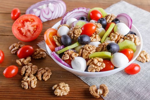 Salad with fresh cherry tomatoes, mozzarella cheese, olives, kiwi, onion and walnuts on brown