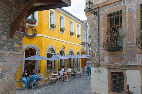 Busy people sitting in front of historic buildings under parasols in an old town alley, Xanthi,