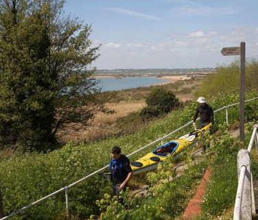 Two men carrying a canoe down to the beach, West Mersea, Mersea Island, Essex, England, United