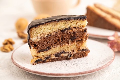 Chocolate biscuit cake with caramel cream and walnuts, cup of coffee on gray concrete background.