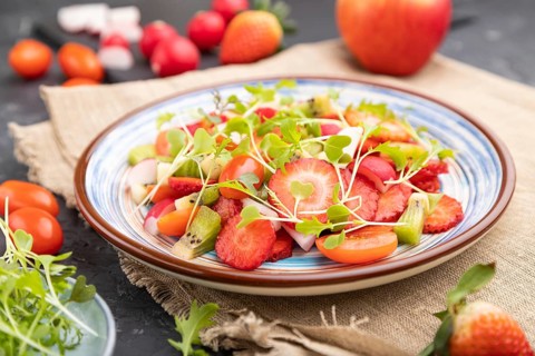 Vegetarian fruits and vegetables salad of strawberry, kiwi, tomatoes, microgreen sprouts on black