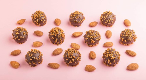 Chocolate caramel ball candies with almonds in a row on a pastel pink background. side view, close