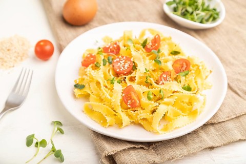 Reginelle semolina pasta with tomato, eggs, sesame and microgreen sprouts on a white wooden