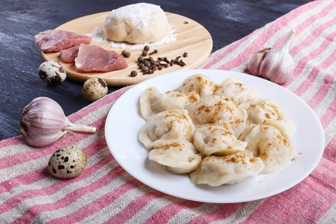 Dumplings on a plate with ingredients (meat, dough, spices) on a linen tablecloth on a black wooden