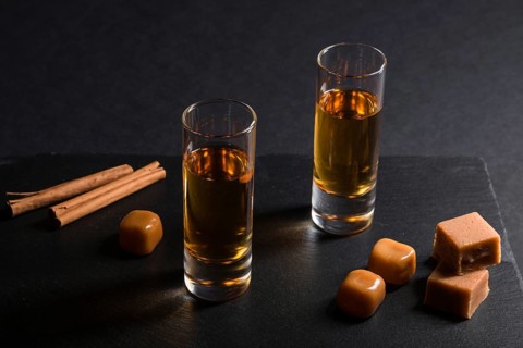 Glass of whiskey with caramel candies on a black stone slate board on black background. Side view,