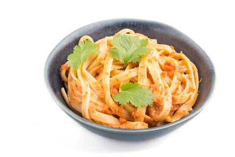 Semolina pasta with tomato pesto sauce, orange and herbs in bowl isolated on white background. Side