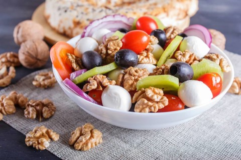 Salad with fresh cherry tomatoes, mozzarella cheese, black olives, kiwi, onion and walnuts on black
