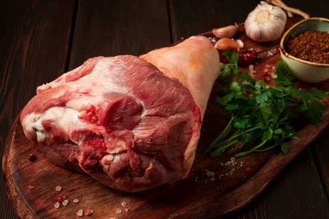 Raw pork knuckle, on a wooden chopping board, with spices, close-up, top view, no people