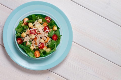 Classic Caesar salad, with cherry and croutons, top view, on a white table, horizontal, no people