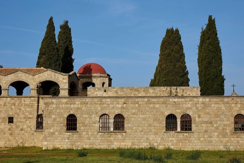 Monastery of Our Lady of Mount Filerimos, Historic stone wall with round windows and tall cypresses