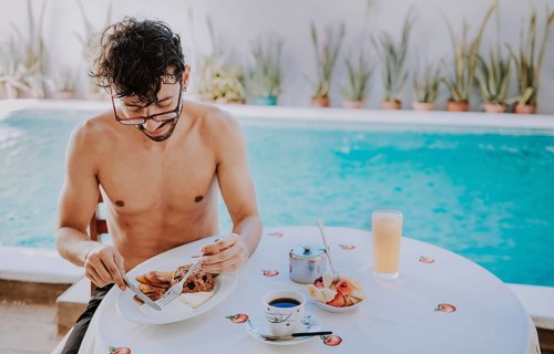 Young man on vacation in hotel having breakfast near swimming pool. Breakfast near the swimming