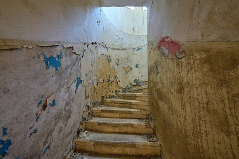 Dilapidated staircase with peeling paint and round window through which light enters, Lost Place,