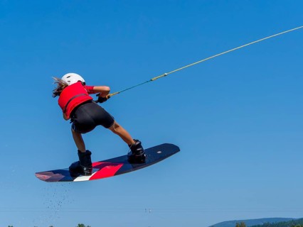 Boy or girl, jump with wakeboard over the lake, red life jacket and water sports, water skiing in