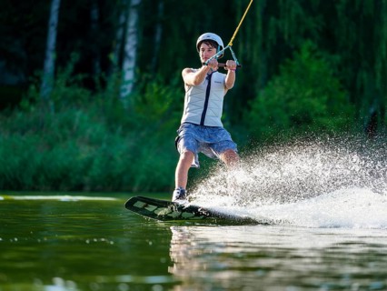 Sporty young man with helmet and waistcoat on wakeboard in lake, water sports, water skiing in