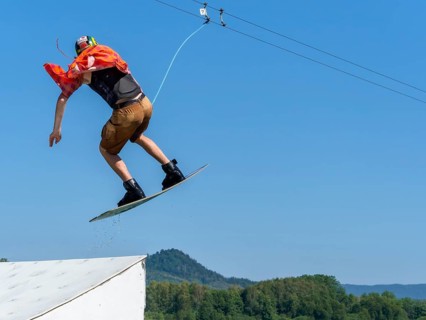 Young casual man with flapping shirt on wakeboard jumping over jump into the lake, water ski and