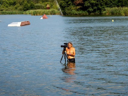 Cameraman and photographer with swimming trunks and tripod in the lake, water skiing and wake park,
