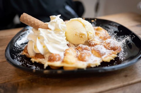 Belgian waffle with vanilla ice cream and whipped cream, waffle rolls, arranged on a black plate