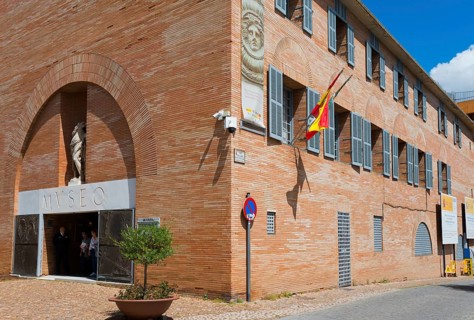 Red brick museum building with Spanish flag and sculptures at the entrance, Museo Nacional de Arte