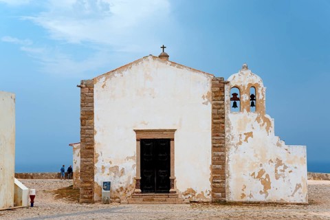 A historic chapel with bell tower and views of the ocean, surrounded by ancient walls, Igreja de