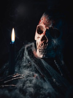 Skull with traces of blood and cobwebs, next to a candle in a dark environment