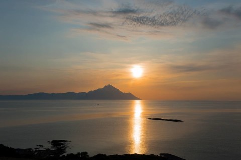 The sun rises, illuminating the sea and an island in the distance, view of Mount Athos, Orthodox
